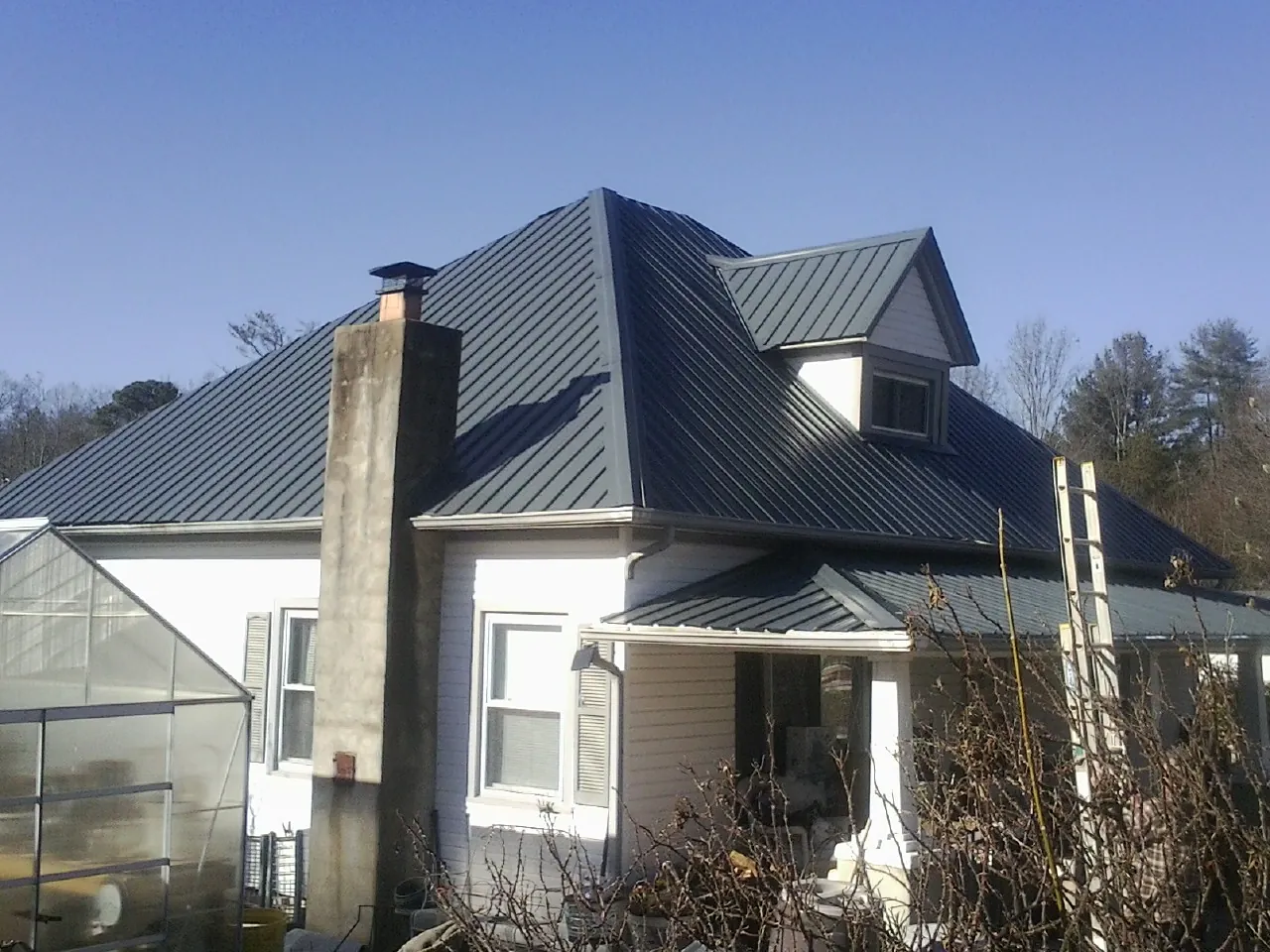 Dark blue standing seam metal roof on a white farmhouse with dormer — Slate & Tile Roof Repair by Roofing Brothers in Nora Springs