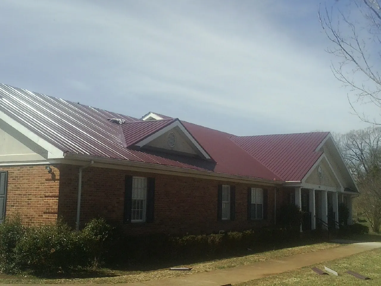 Red metal roof with gabled entries on a long brick building, from a Hail Damage Roof Repair job in Nora Springs