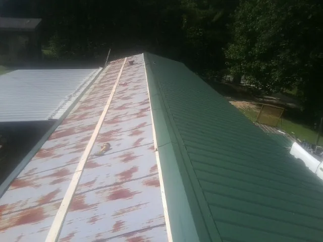 Old rusted panels beside newly installed green metal roofing — Wind Damage Roof Repair by Roofing Brothers in Nora Springs