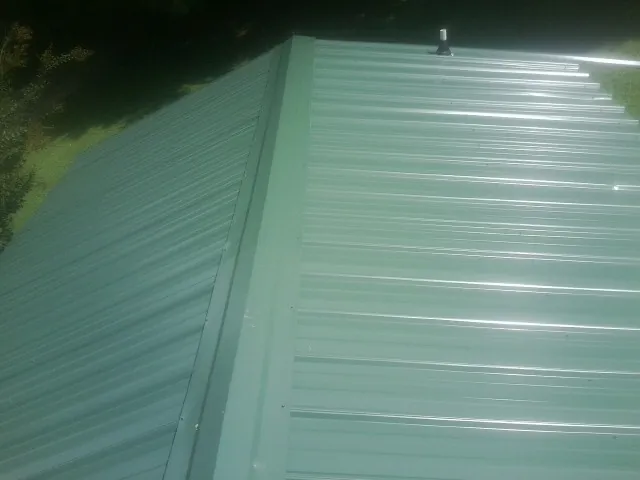 New green metal panels meeting at the ridge of a roof — Flat Roof Repair work by our crew in Nora Springs