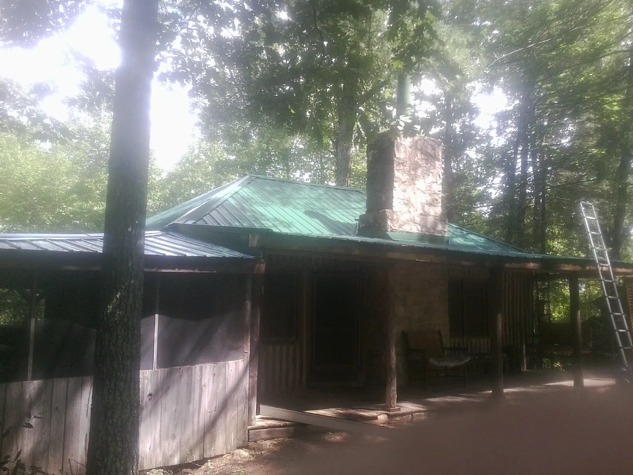 Green metal roof and stone chimney above a log cabin porch in Nora Springs