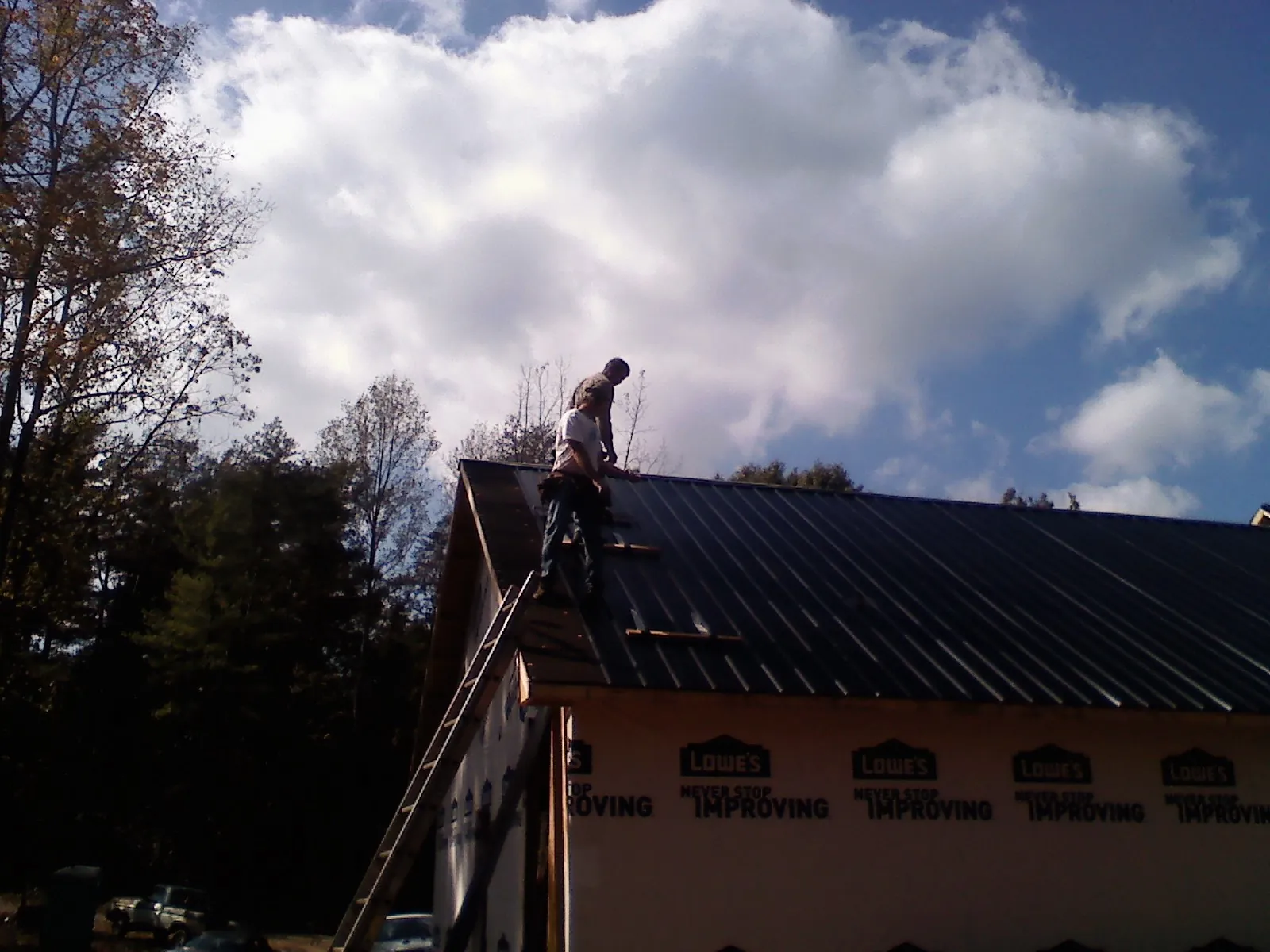 Roofer fastening dark metal panels high against a cloudy sky, from a Roof Inspection job in Nora Springs