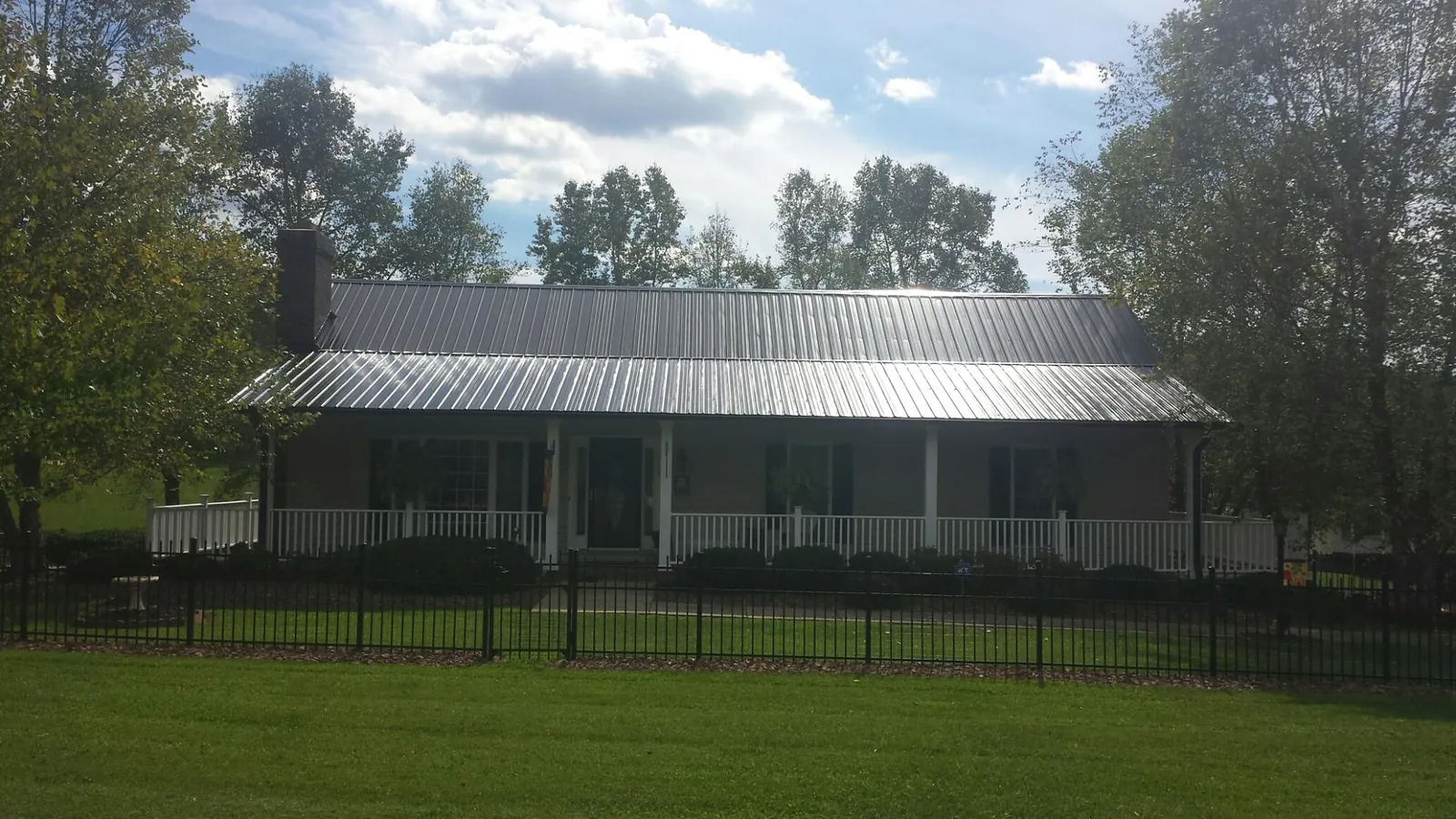 Gray metal roof on a brick ranch with a full width front porch — Gutter Guard Installation work by our crew in Nora Springs