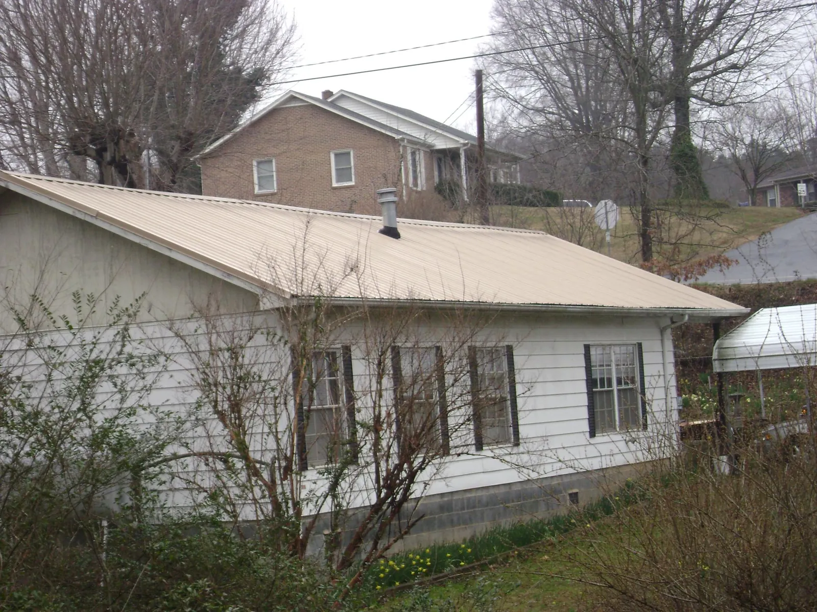 Tan metal roof on a white sided house set into a hillside — Commercial Roofing by Roofing Brothers in Nora Springs