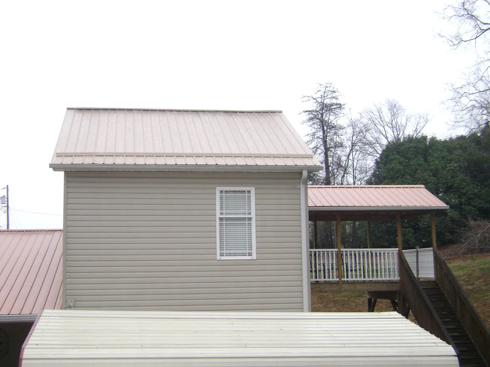 Tan metal roofs on a two story addition and attached porch, from a Roof Replacement job in Nora Springs