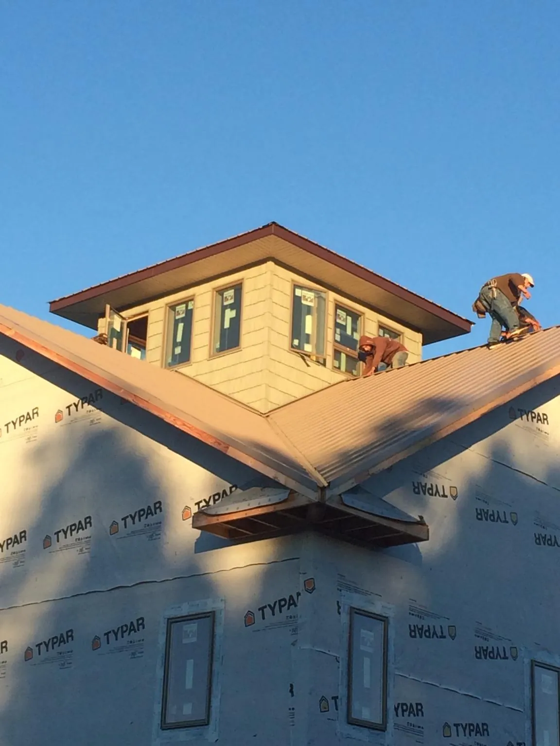 Roofers working around a rooftop cupola on a new metal roof at sunset — Roof Waterproofing in Nora Springs by Roofing Brothers